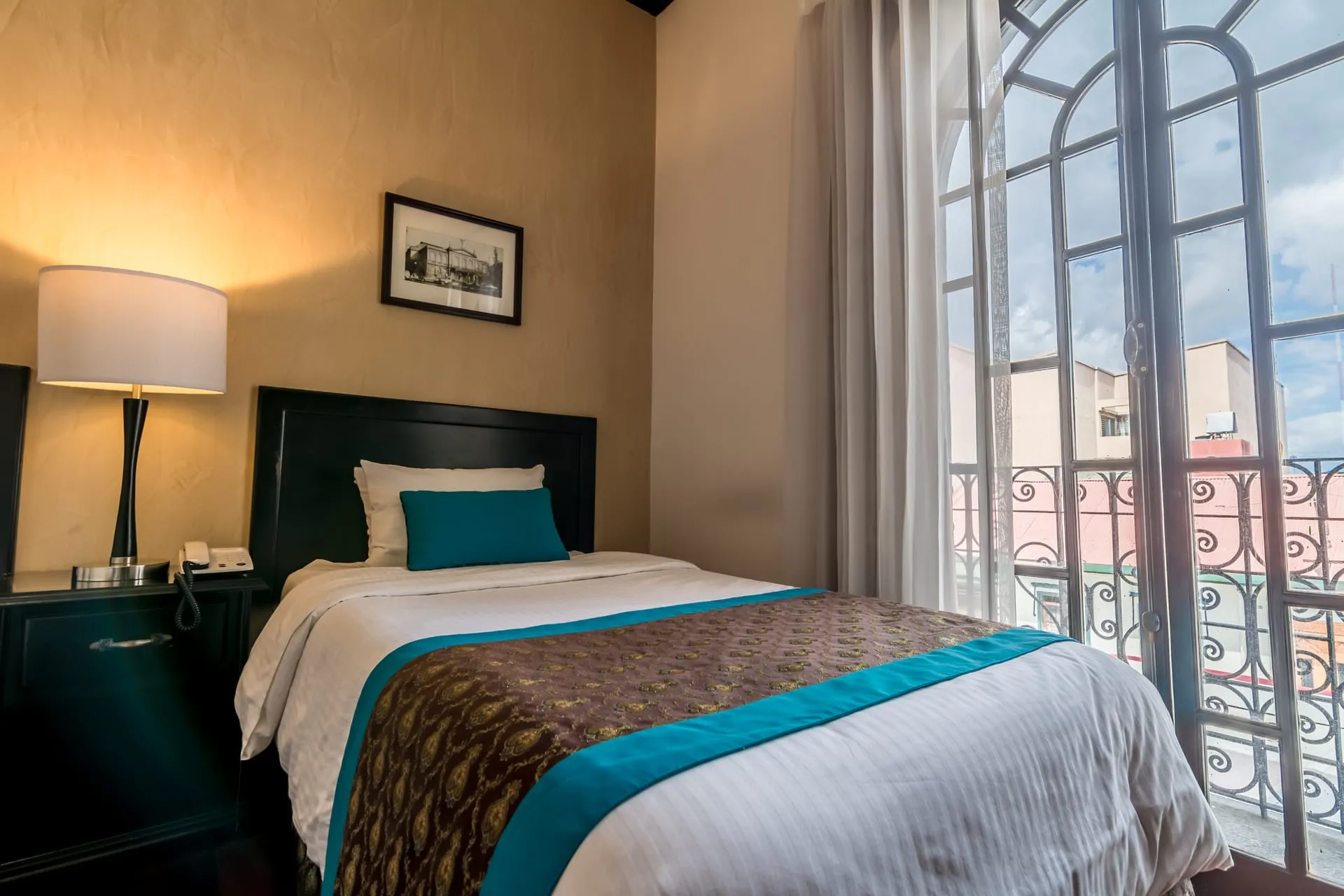 Cama individual de la Habitación Triple junto a un balcón con vista a los tejados josefinos
